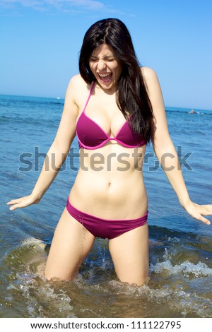 Woman with fantastic body screaming in the cold water on the beach