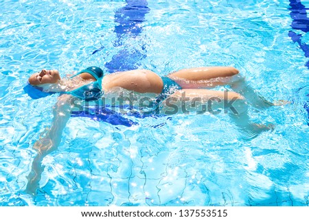 Happy relaxed pregnant woman swimming happy in beautiful swimming pool