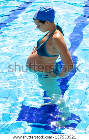 Happy beautiful pregnant woman watching her big belly in the water