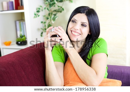Beautiful female model holding mug of coffee at home on sofa