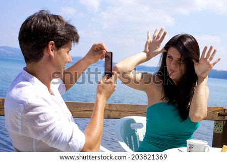 Handsome man taking picture with mobile phone of girlfriend making funny faces