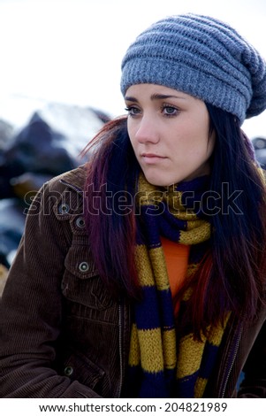 Young female model posing sad in front of rocks