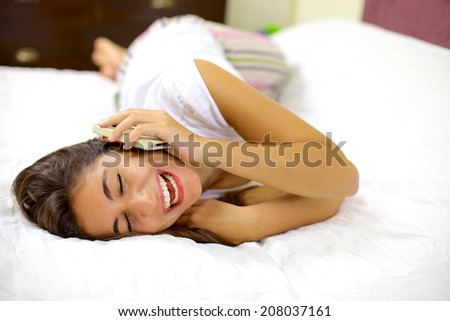 Happy woman smiling on the phone laying in bed
