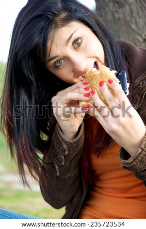 Young woman eating hamburger bread with iphone inside