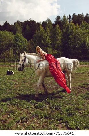 Beautiful blond woman in red dress on a white horse