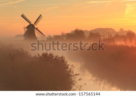 Foggy sunrise in a wetland near a traditional windmill in Holland.