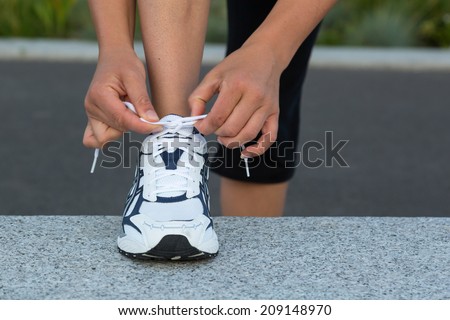 Closeup of female hands tying running shoes laces on a wall before training.