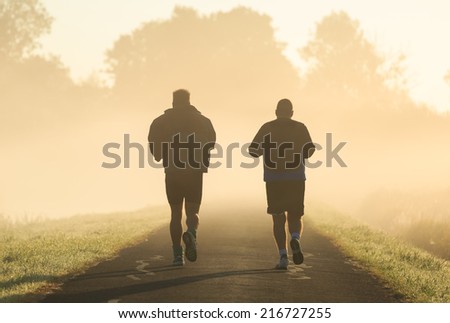 Two middle aged men running in the morning fog.