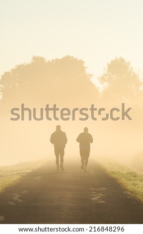 Two men running in the fog on a beautiful morning.