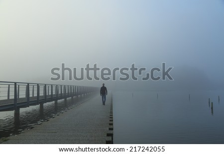 Man walking into the morning fog on a jetty.