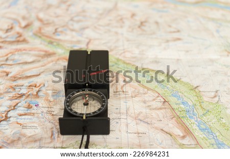 Modern compass on a topographical map of a mountain range.