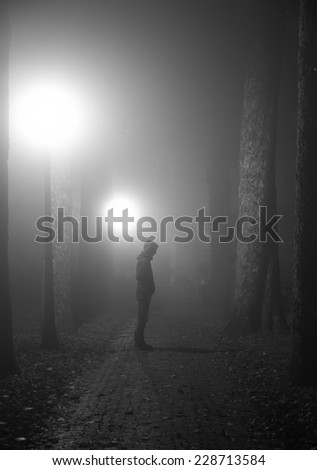 Scary man standing in a lane on a foggy night. Black and white.