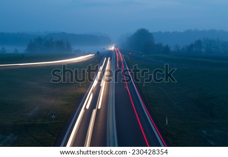 Traffic on a single lane road at a foggy evening.