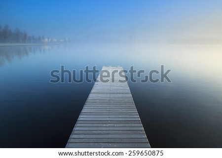 Empty jetty in a foggy lake during a cold sunrise.