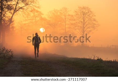 Athlete running on a gravel road during a foggy, spring sunrise in the countryside, with the sun in the background.