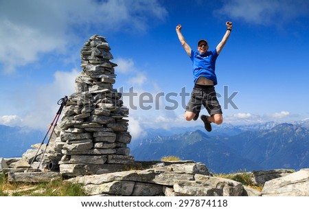 Man reaching the summit and jumping out of joy beside a big cairn on a mountaintop.