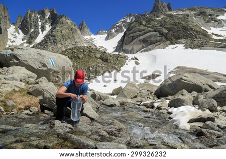 Female hiker taking in water from river in the mountains after hiking. Enjoying outdoors summer trekking vacation.