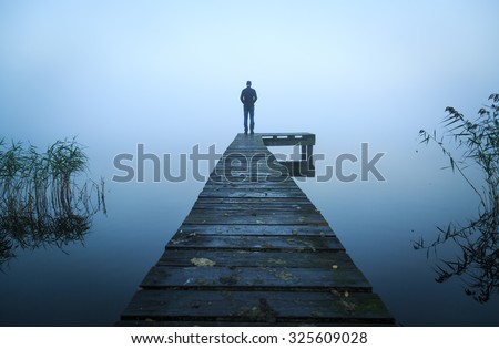 Depressed emotions concept: man standing at the end of a jetty, on a foggy, autumn morning.