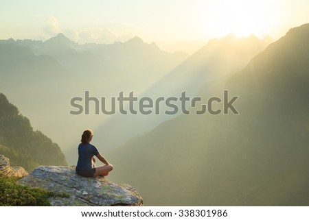 Woman sitting on a rock, enjoying the summer sunset in the mountains.