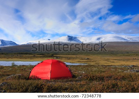 Camping with a red tent in Arctic  wilderness with snow capped mountains.