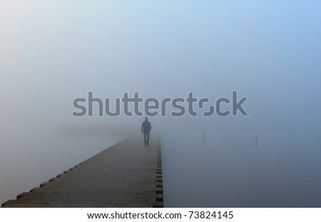 Man walking into the fog on a jetty.
