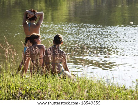Three girls sitting at bank of river
