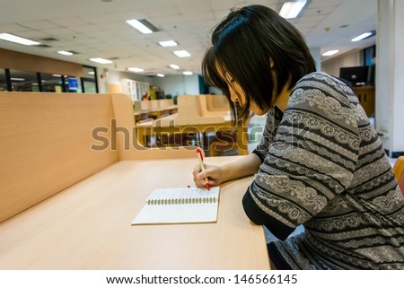 Asian Thai college girl student is writing her diary note book or doing research on a clean desk in the library university