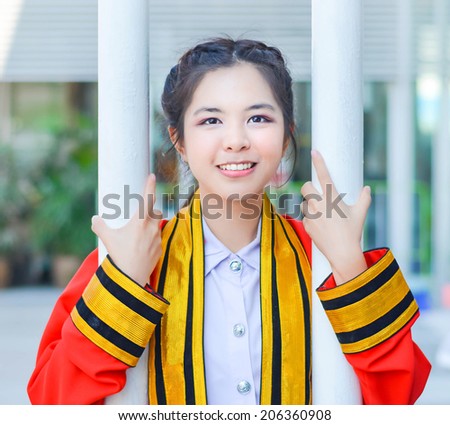 Graduate Thai college girl in academic gown is holding poles and smiling happily for the moment