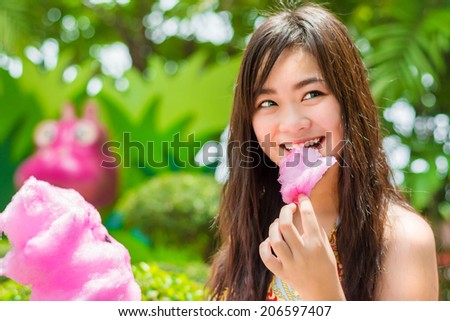 Cute Asian Thai girl is eating pink candyfloss with joy in bright summer in nature green background concept version