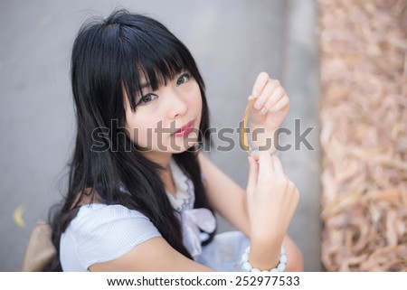 A cute Asian Thai girl is holding a dry leaf and making eye contact