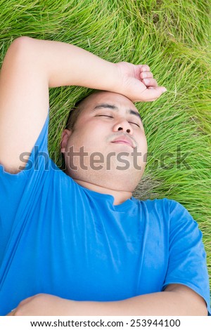 Stressful fat man is lying on the green grass with arm on his head