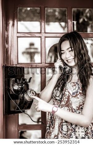 Thai girl is talking with an old-fashion phone in the telephone booth in black and white retro style