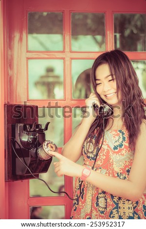 Thai girl is talking with an old-fashion phone in the telephone booth in soft vintage color style