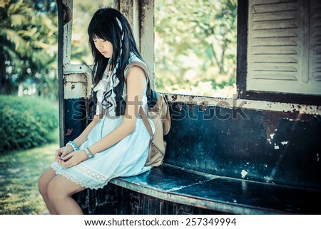 Cute Asian Thai girl in vintage clothes is waiting alone in an old bus stop in vintage color tone