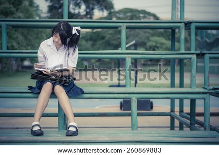 Cute Asian Thai schoolgirl student in uniform is sitting and reading on a metal stand reading books in vintage color