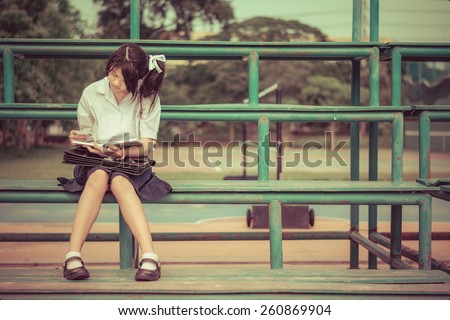 Cute Thai schoolgirl is sitting and reading on a stand in vintage color