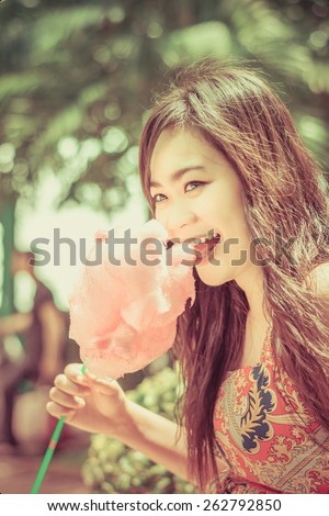 Cute Asian Thai girl is eating pink candyfloss with joy in bright summer in nature green background concept version in vintage color