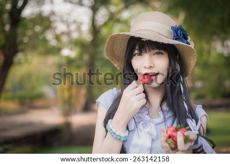 A cute Asian Thai girl with vintage clothing is eating strawberry she picked up in the forest
