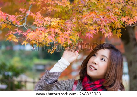 Cute Asian Thai girl is touching red leaves in autumn season above her head. This is Japanese concept picture.