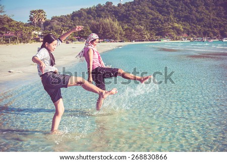 Two Asian Thai girls are kicking the sea along the beach coast of Rayong, Thailand in vintage color