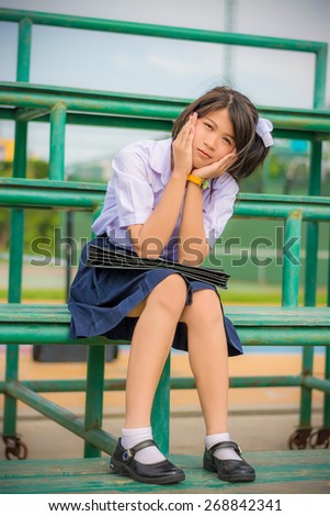 Shy Asian Thai schoolgirl student in uniform sitting on a metal stand in childhood theme. She is bashful.