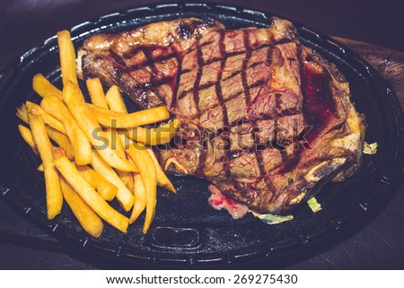 Premium American prime rib steak with french fries on a metal plate ready to serve. The focus is shallow depth of field.