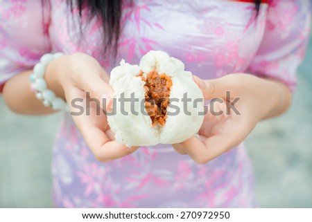 Chinese girl in cheongsam is tearing steamed stuff bun. Steamed stuff bun is one of Chinese dumpling cuisine. Focus on the dumpling bun
