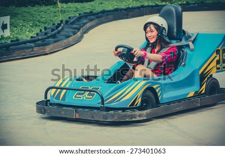 Cute Asian Thai girl is driving Go-kart car with speed in a playground racing track in vintage color. Go kart is a popular leisure motor sports.