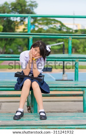 Asian Thai schoolgirl student in high school uniform education fashion is sitting on a metal stand and showing annoying sulk facial expression. She kept something in mind and not in good mood.