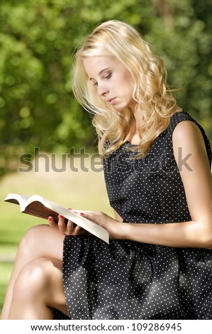 Young pretty blonde woman reading book in park outdoor