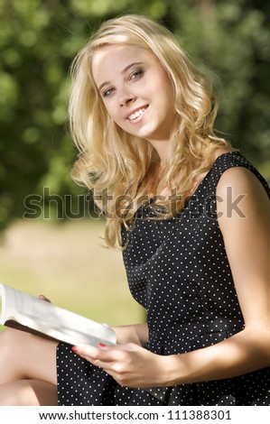 Young attractive blonde woman reading book in park outdoor