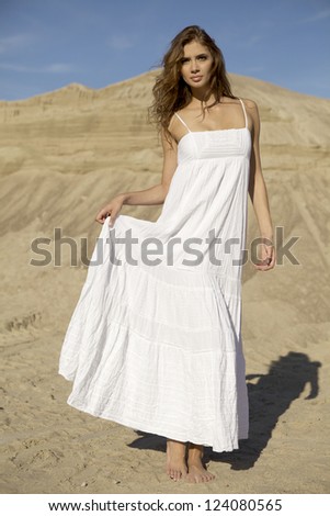 Fashionable young attractive and sensuality brunette woman in white dress dancing on the desert