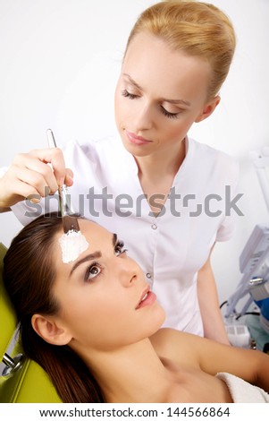 young woman getting beauty skin mask treatment on her face with brush