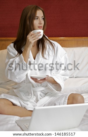 Portrait of beautiful young adult attractive sensuality brunette woman with white cup and laptop on bed at bedroom in luxury apartment